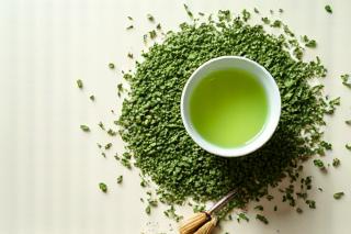 Friss zöld tea levelek kis gőzölgő csészék mellett